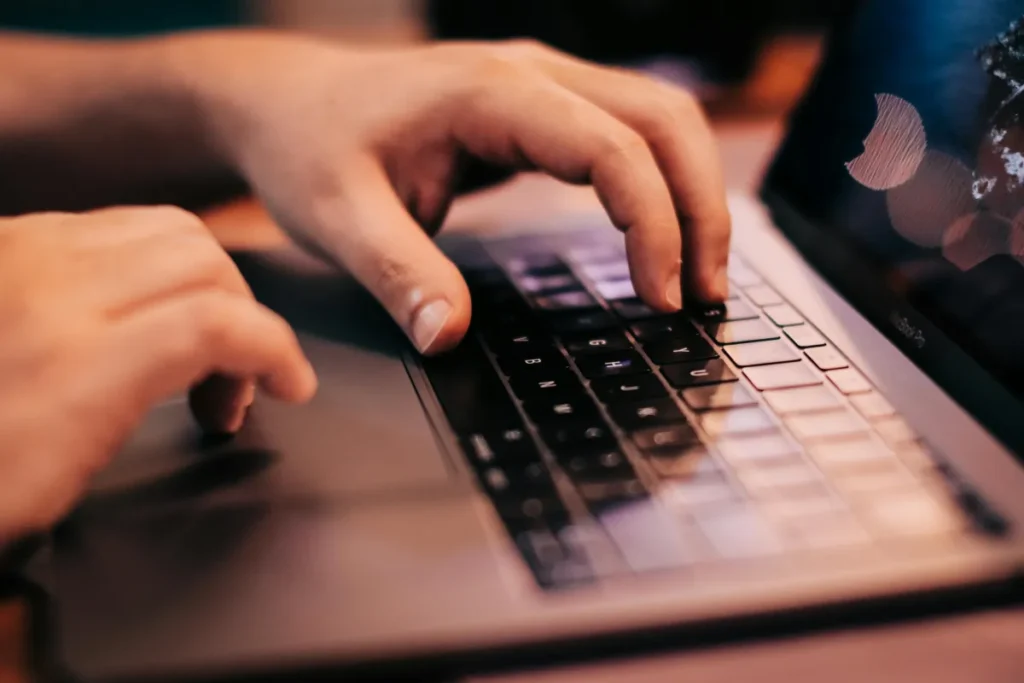 Tangan seseorang mengetik di keyboard laptop saat bekerja di depan komputer